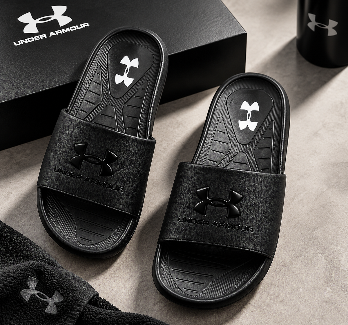Pair of black Under Armour men's slides on grey stone