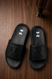 Black Under Armour slides on a wooden floor